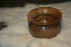 a small wooden bowl sitting on top of a white fur covered floor next to a metal object