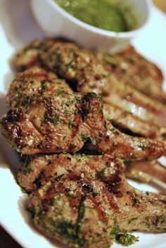 grilled meat and vegetables on a white plate with dipping sauce in a small bowl