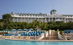 an outdoor swimming pool next to a large white building with blue umbrellas and lawn chairs