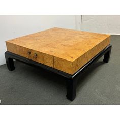 a coffee table made out of wood with black legs and drawers on the top, sitting in an empty room