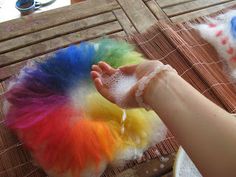 someone is washing their hands with soap and rainbow colored hair on top of a table