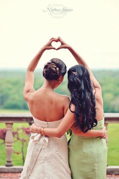 two women standing next to each other with their hands in the shape of a heart