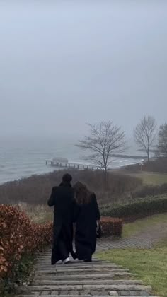 two people are walking down some steps towards the ocean on a foggy, overcast day