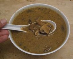 a hand holding a spoon full of soup with mushrooms on it and broth in the bowl