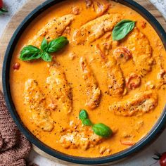 a skillet filled with chicken and tomato sauce, garnished with basil leaves