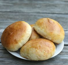 four rolls on a white plate sitting on a wooden table