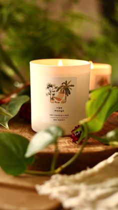 a white candle sitting on top of a wooden table next to green plants and leaves