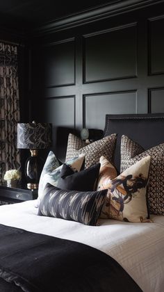 a bed with black headboard and pillows in a room that has dark wood paneling on the walls