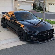 a black mustang parked in front of a house with orange flames painted on the hood