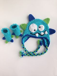 a crocheted blue hat with green leaves on it and two little monsters attached to it