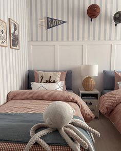 two beds in a room with striped wallpaper and an octopus stuffed animal on the bed