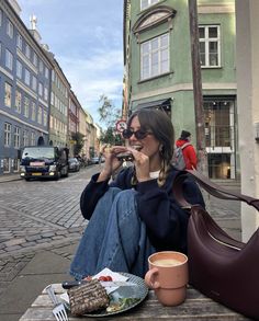 a woman sitting on a bench eating food and drinking coffee