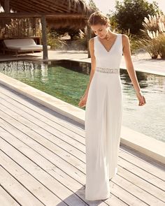 a woman in a white dress is standing on a wooden deck near the water and looking down