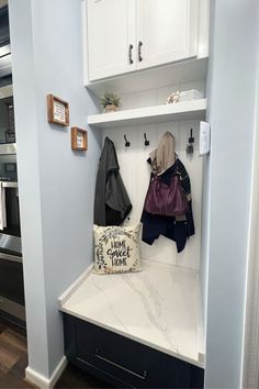 a purse and coat hang on a white shelf in a blue walled entryway to a kitchen