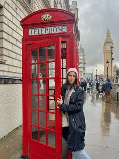 a woman standing next to a red phone booth