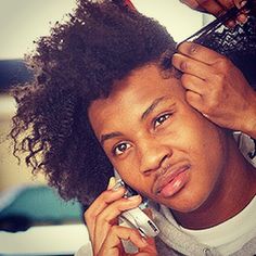 a woman talking on a cell phone while getting her hair styled by another person with an afro