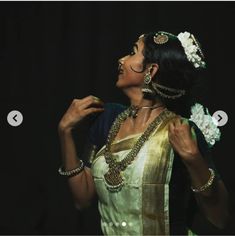 a woman in a white and gold sari with jewelry on her neck, standing against a black background