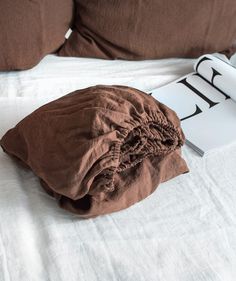 an unmade bed with two pillows and a book on the pillowcase next to it