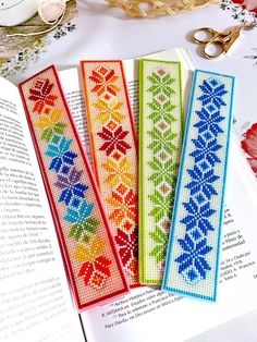 four cross stitch bookmarks sitting on top of an open book