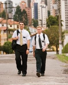 two men walking down the street with backpacks on their back and one man in white shirt and tie