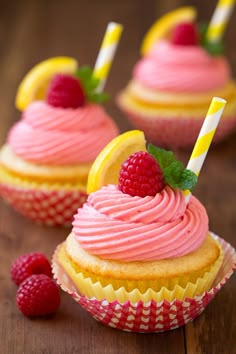 three cupcakes with pink frosting and raspberries on the top one has a lemon slice