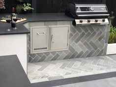 an outdoor kitchen with a grill and wine glasses on the counter