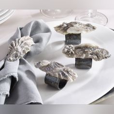 four pieces of raw oyster on a white plate with silverware and wine glasses in the background