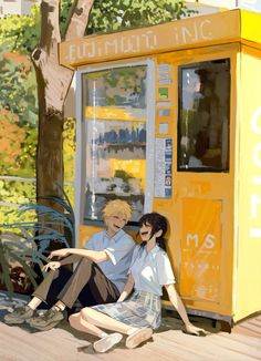 two people sitting on the ground next to a yellow phone booth with trees in the background