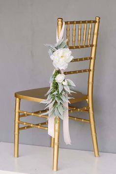 a gold chair decorated with flowers and greenery for a wedding or special event, against a gray background