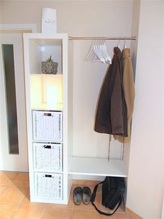 a white shelf with baskets and shoes next to a coat rack in a room that has tile flooring