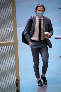 a man wearing a face mask walks down the street while holding a cup of coffee