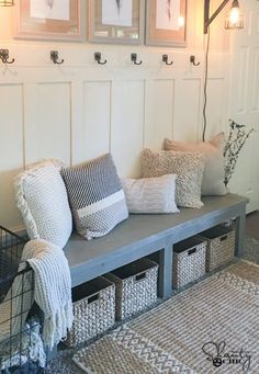 a bench with some pillows on it in front of two pictures and a basket under the bench