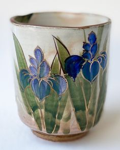 a close up of a cup on a white surface with blue flowers and green leaves