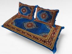 two pillows on top of each other with blue and red designs in them, sitting on a white surface