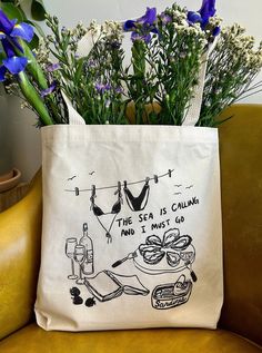 a tote bag sitting on top of a brown chair next to flowers and bottles