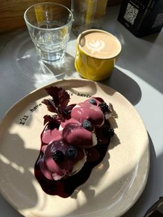 a white plate topped with fruit covered in blueberries next to a cup of coffee