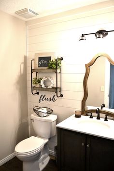 a white toilet sitting next to a sink in a bathroom under a wooden mirror frame