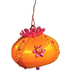 an orange ornament with pink flowers hanging from it's side on a white background