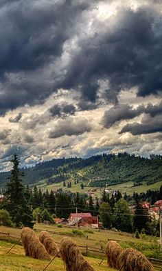 a field with hay bales in the foreground and mountains in the background under cloudy skies