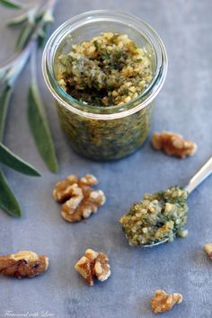 a jar filled with pesto and walnuts next to an olive branch