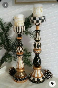 two black and gold candlesticks sitting on top of a table next to pine cones