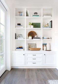 a living room with white bookcases and wood flooring on the side wall