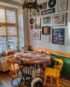 a dining room table with yellow chairs and pictures on the wall above it in front of a window