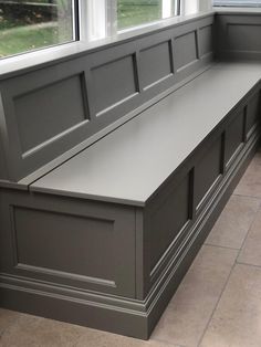 a gray bench sitting in front of two windows next to a tiled floor and wall