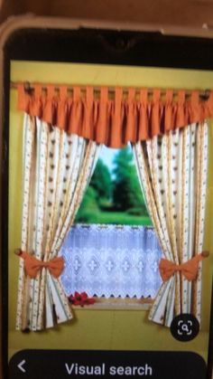 a cell phone showing an image of a window with orange curtains and bows on it