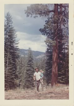 a man holding a child in his arms while standing next to a tall pine tree