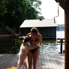 a woman in a bathing suit holding a dog on a dock next to a body of water