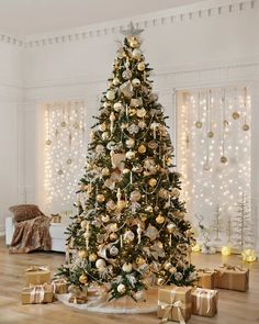 a decorated christmas tree with gold and silver ornaments in a white living room, surrounded by presents