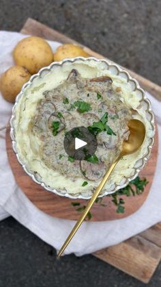 a bowl filled with food sitting on top of a wooden cutting board next to potatoes