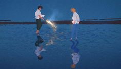 two people are standing in the water and one is holding a sparkler with his reflection